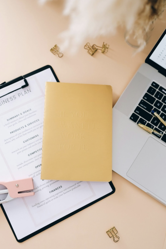 New real estate agent checklist tools: laptop, business plan, and notebook on desk for busy mom realtors getting organized.